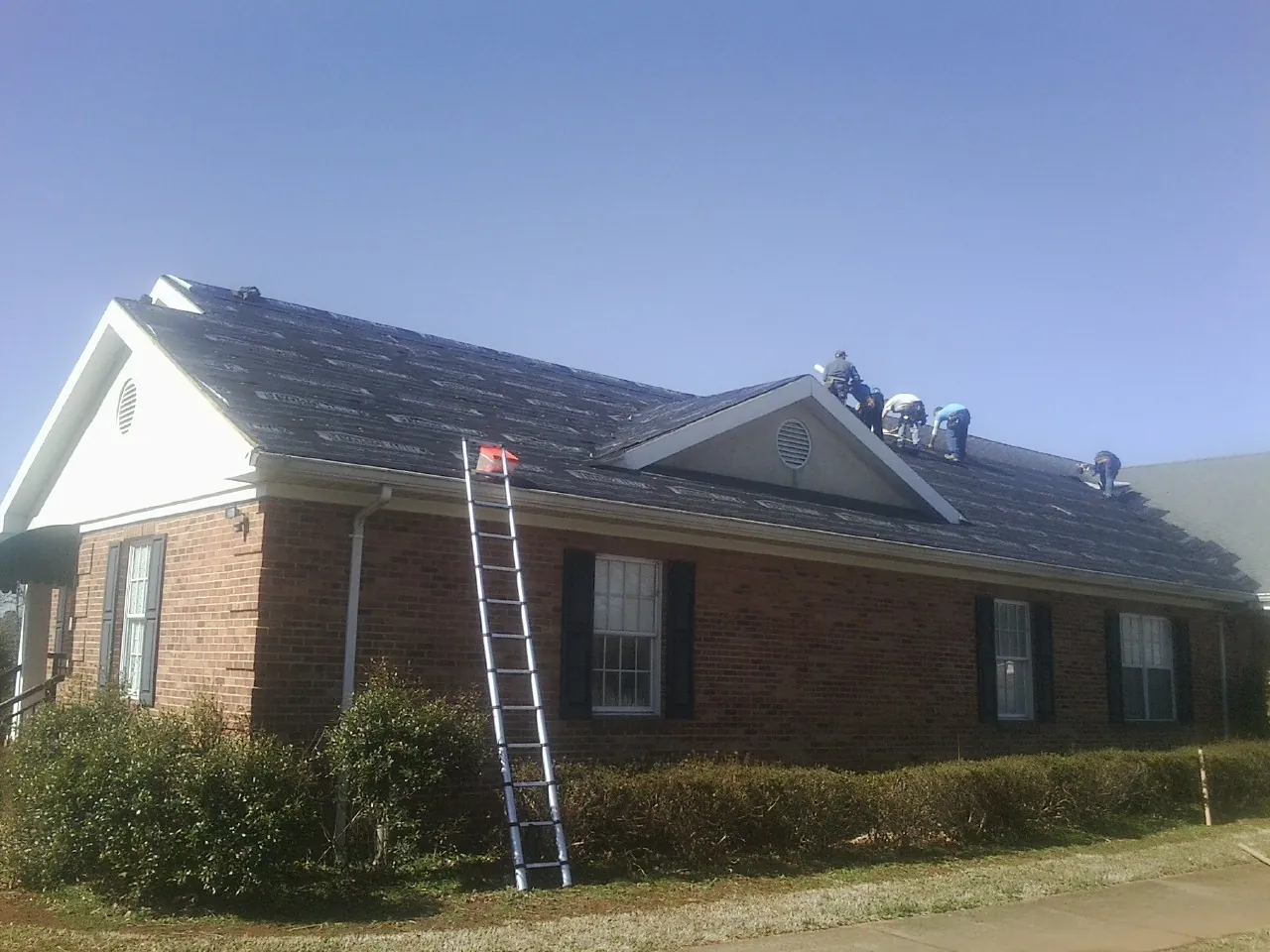 Crew tearing shingles off a brick ranch roof with a ladder set — Emergency Roof Repair work by our crew in Effingham