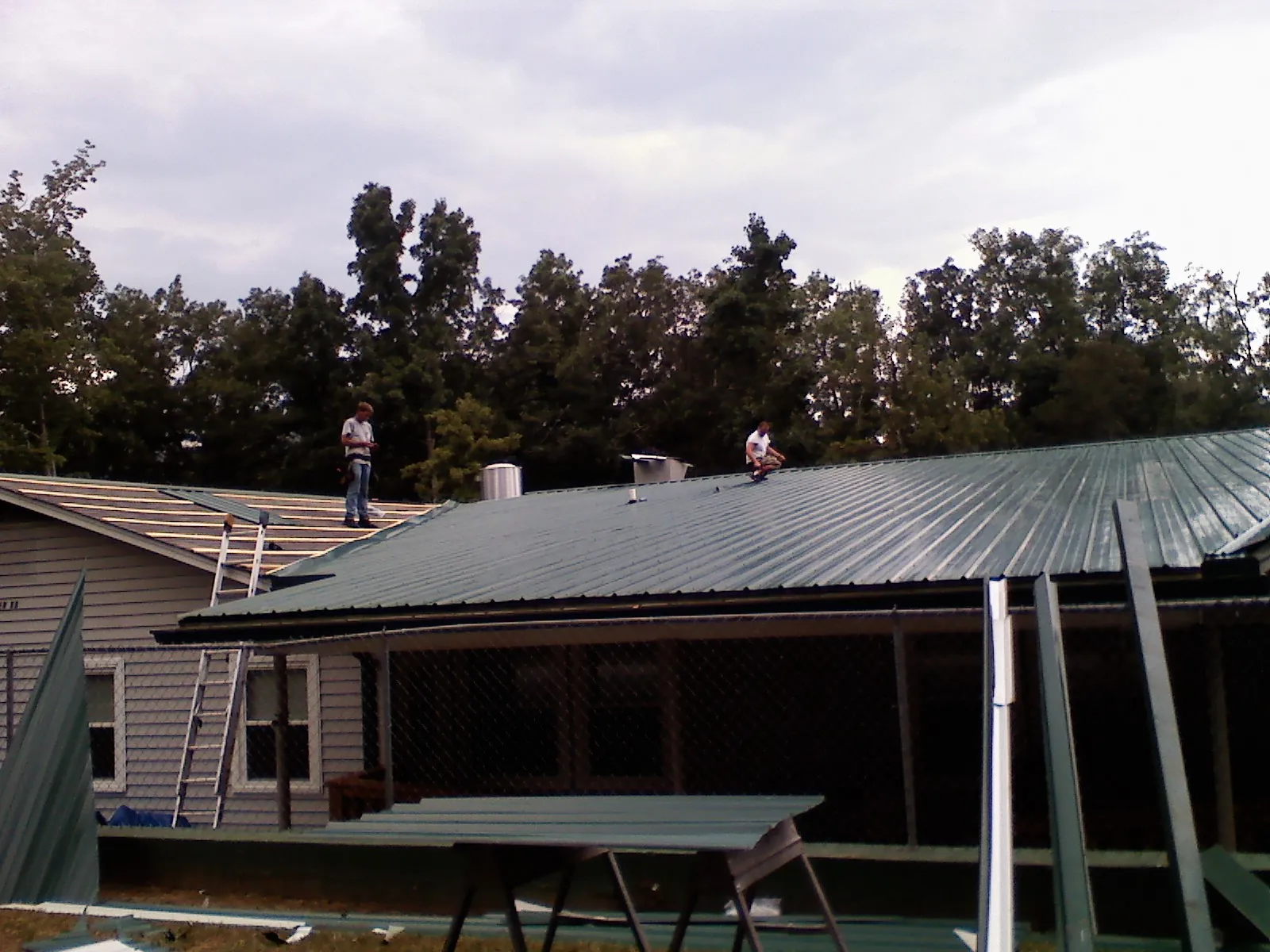 Two roofers installing green metal panels above a covered porch in Effingham